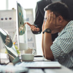 Man at work stressed out as another man stands over him