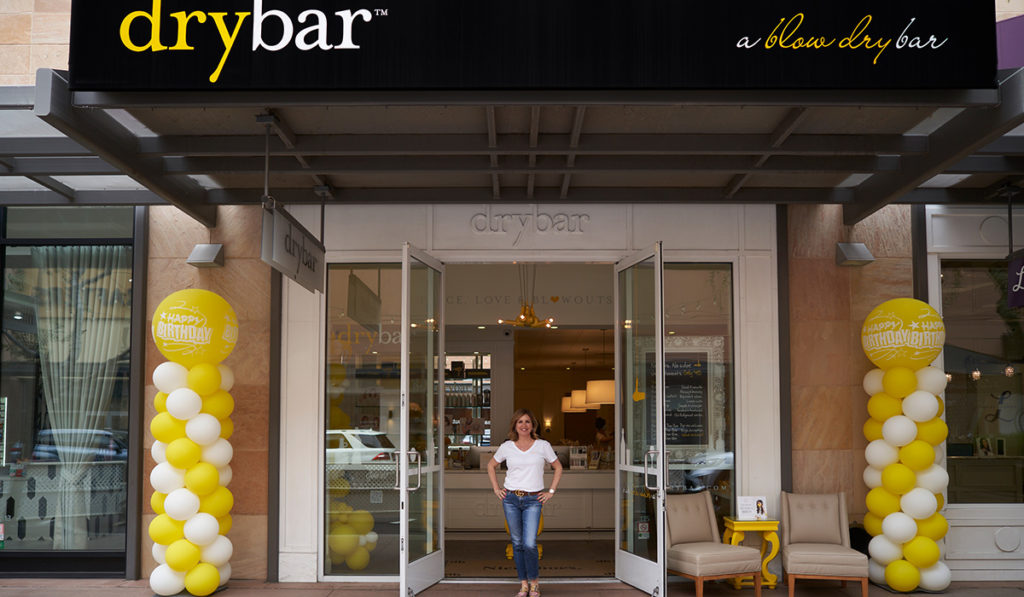 Amy Ross standing in the front entrance of Drybar with 10th Anniversary balloons.